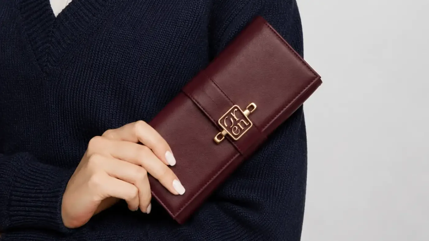Hand holding a burgundy Oren wallet against a navy knit